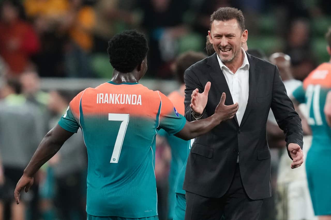 A football player wearing a jersey that says "Irankunda" and the number seven, celebrating with a man in a black blazer and white shirt.