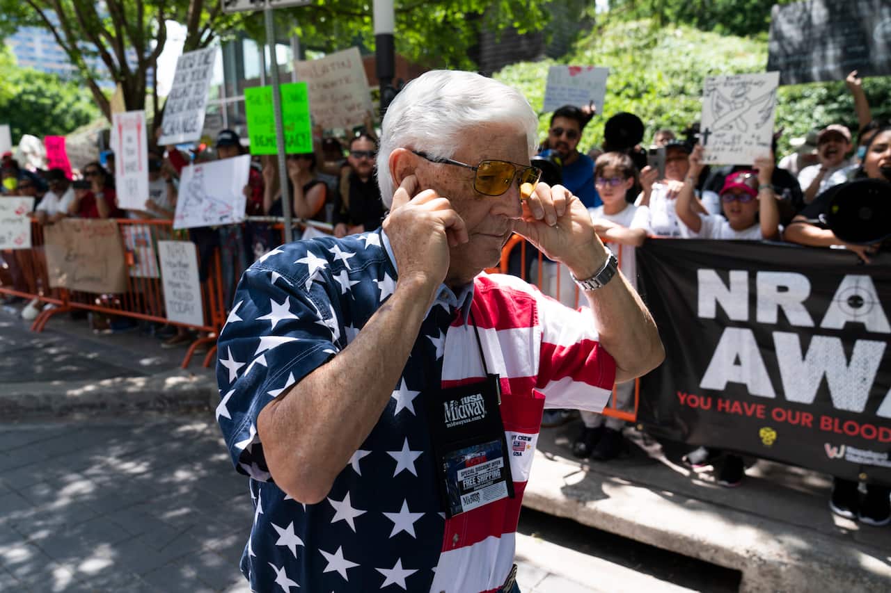 A member of the National Rifle Association plugs his ears with his fingers as he walks past protesters during the NRA's annual meeting in Houston. 