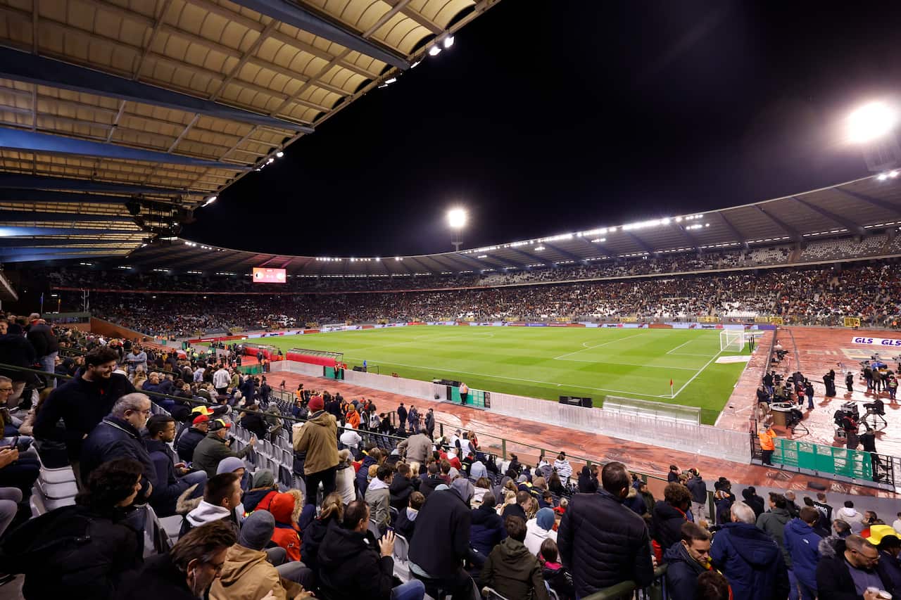 A football pitch at night with large numbers of fans in the stands.