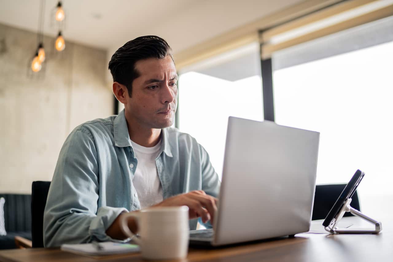 A middle-aged man with dark hair working on a laptop.