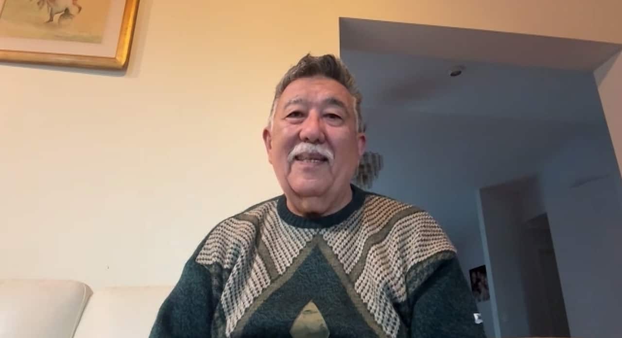 An old man in a green sweater is sitting on a lounge in a living room.