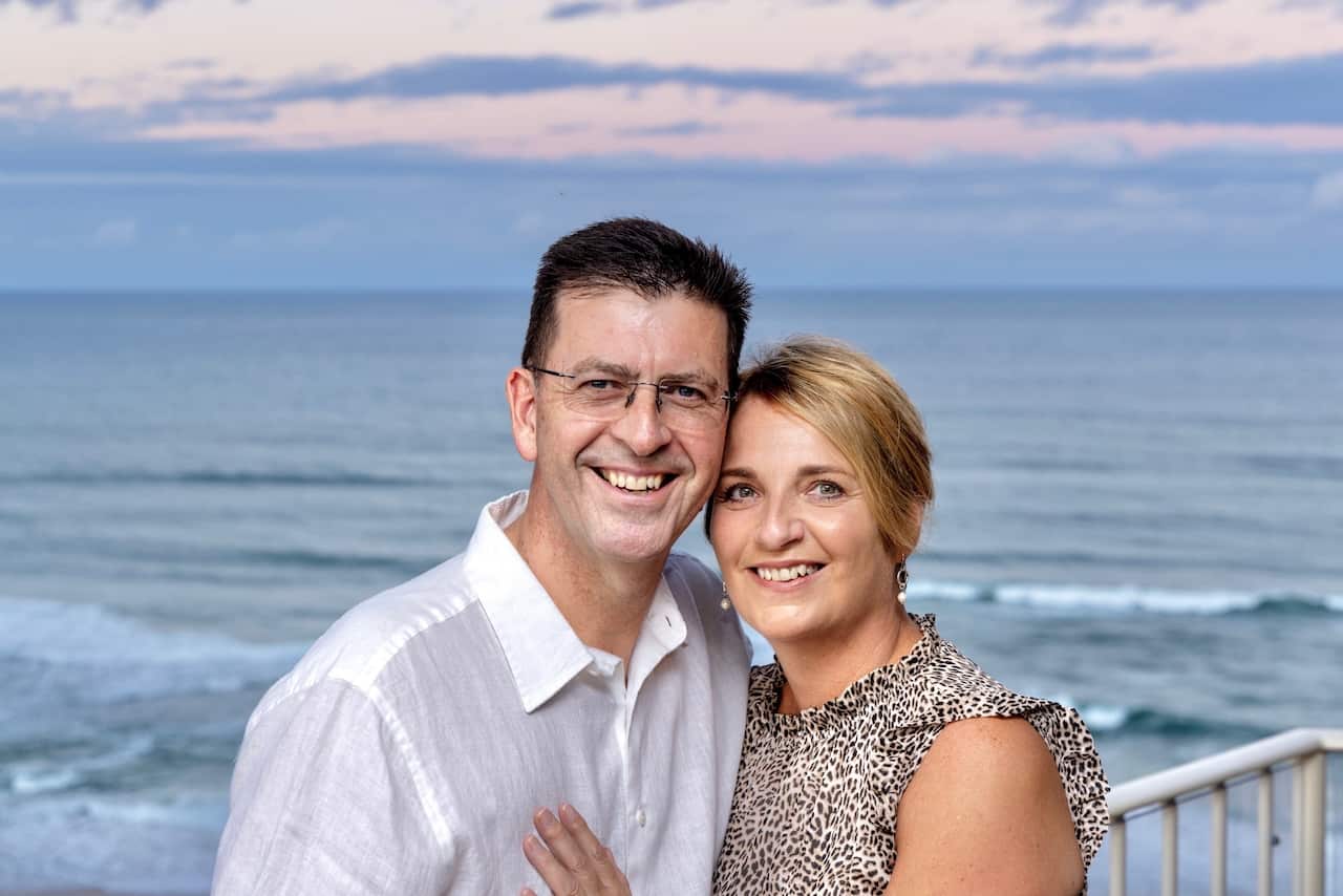 a middle aged couple pose together in front of the sea at sunset