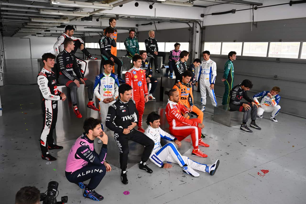 A group of drivers posing together in a grey room.