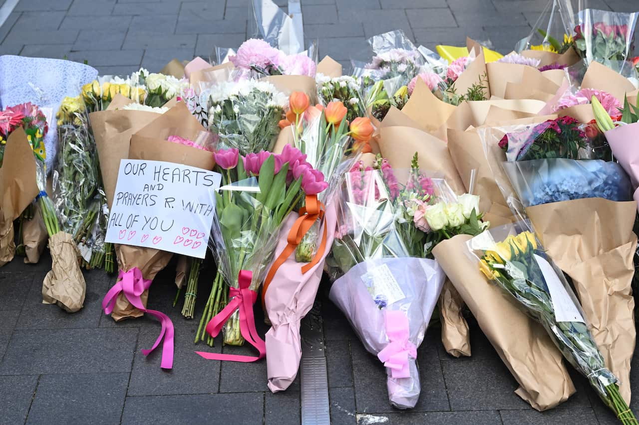 Bunches of floral tributes with a note that reads, "Our hearts and prayers are with all of you".