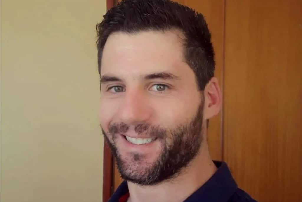 A close-up of a white man with dark hair and a beard smiling.
