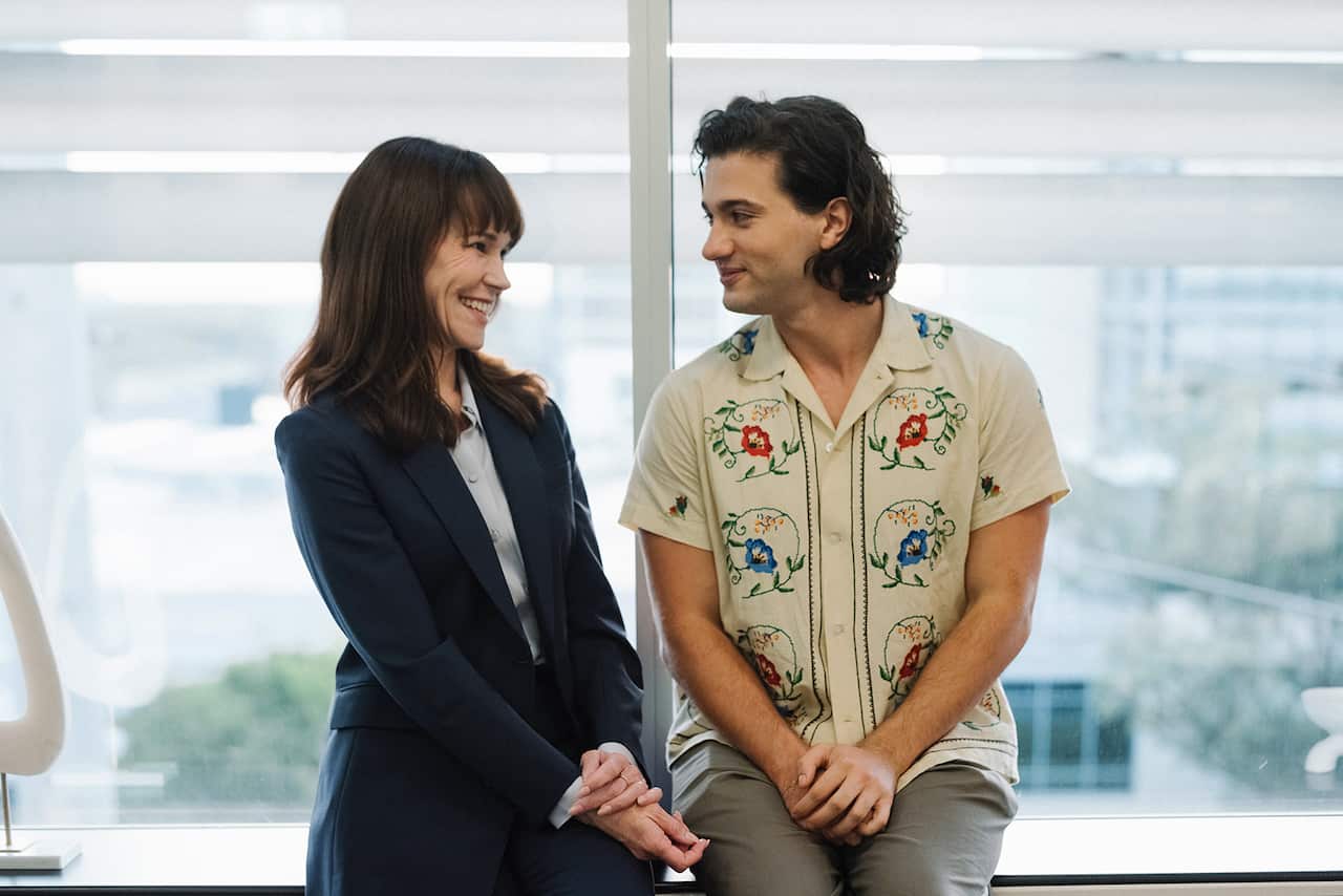 Two people sit on a windown ledge looking at each other and smiling. 