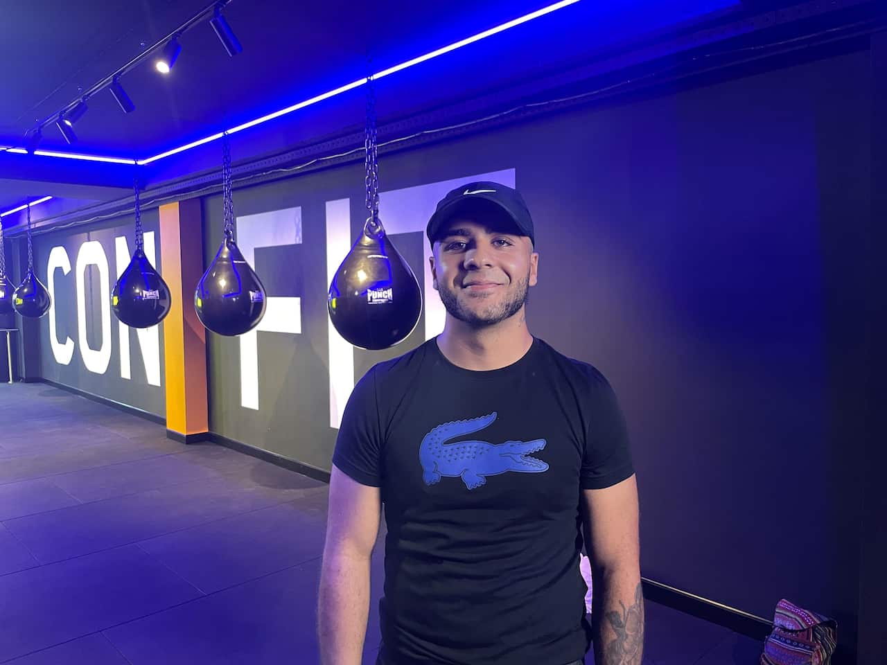 A man wearing a black T-shirt standing inside a gym and posing for a photo.