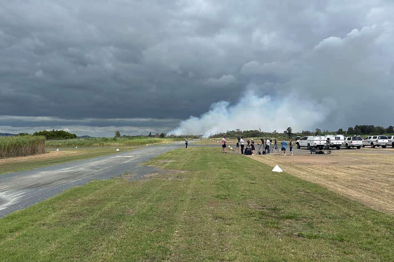 People watching on from an airfield as smoke rises in the distance