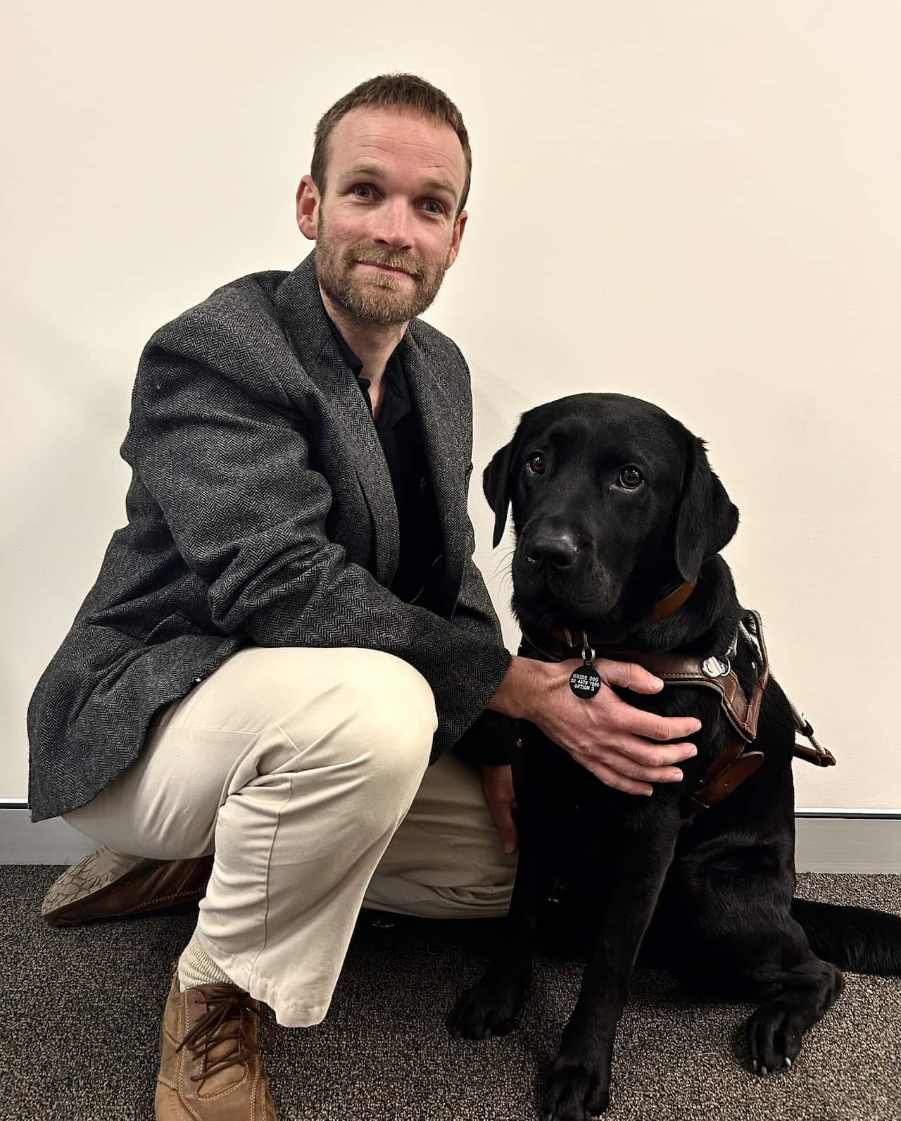  A man crouched next to a guide dog.