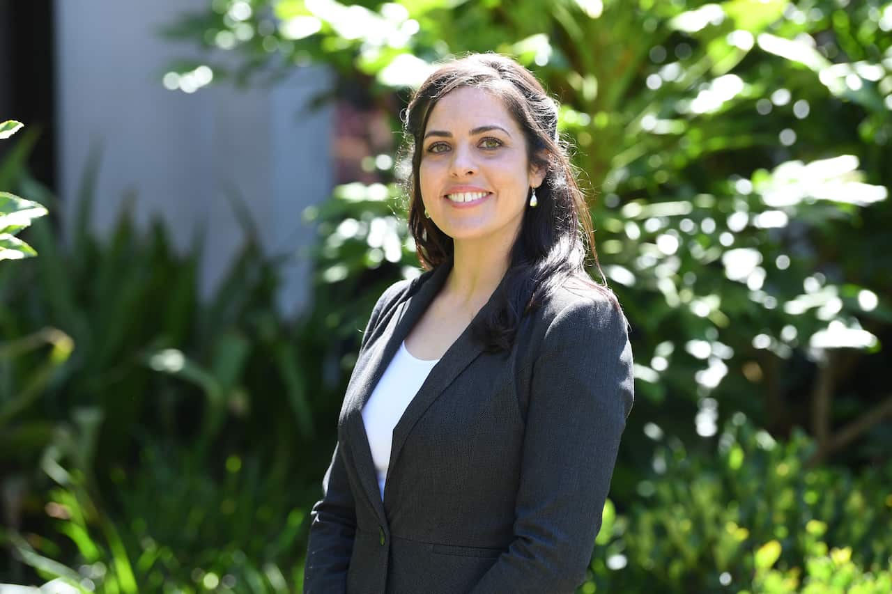 Woman in suit smiles outside by some trees.