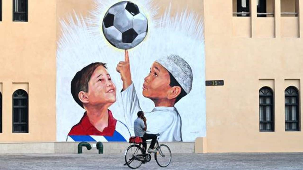 A man rides a bicycle past a mural in Doha.jpg