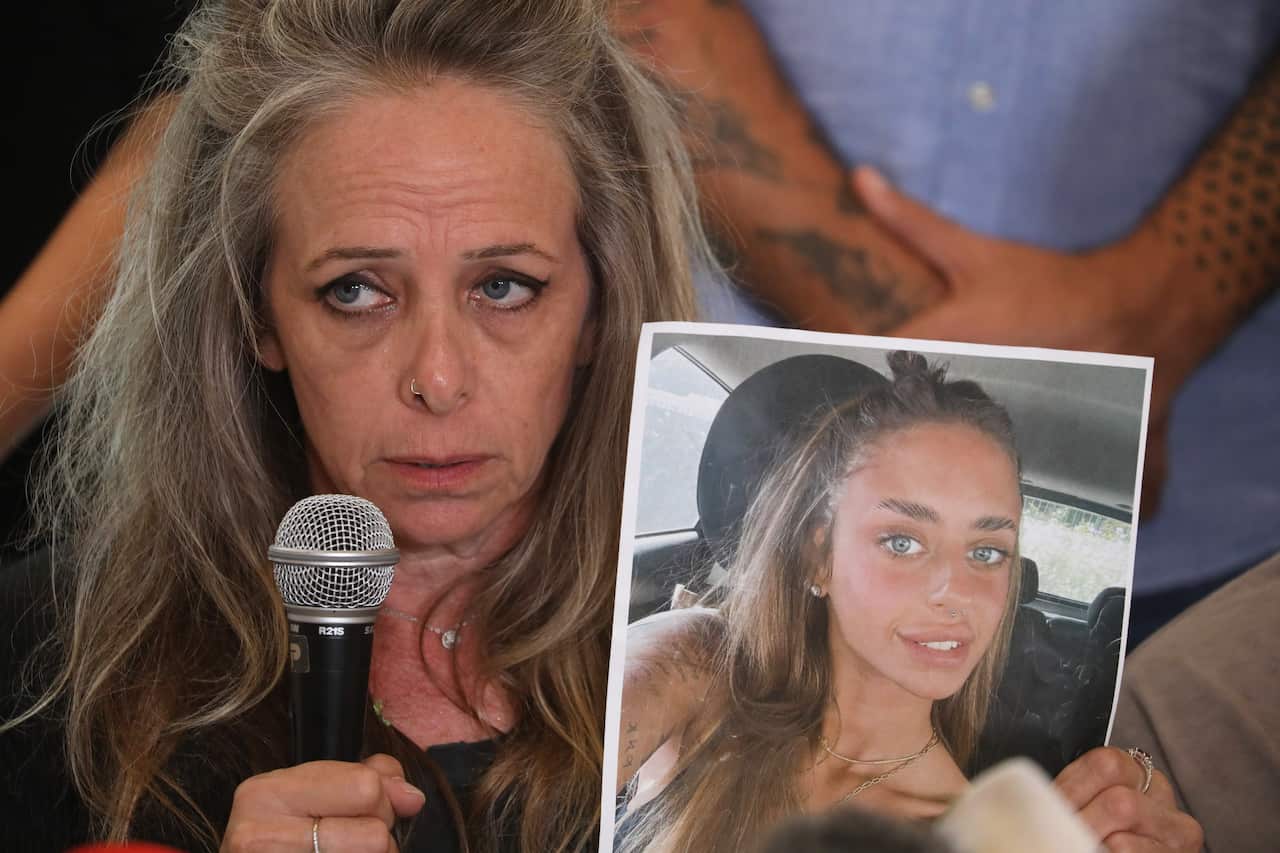A woman holding a microhone and a photo of a smiling girl.