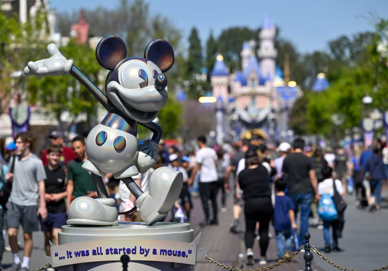 A statue of Mickey Mouse at Disneyland with people in the background.