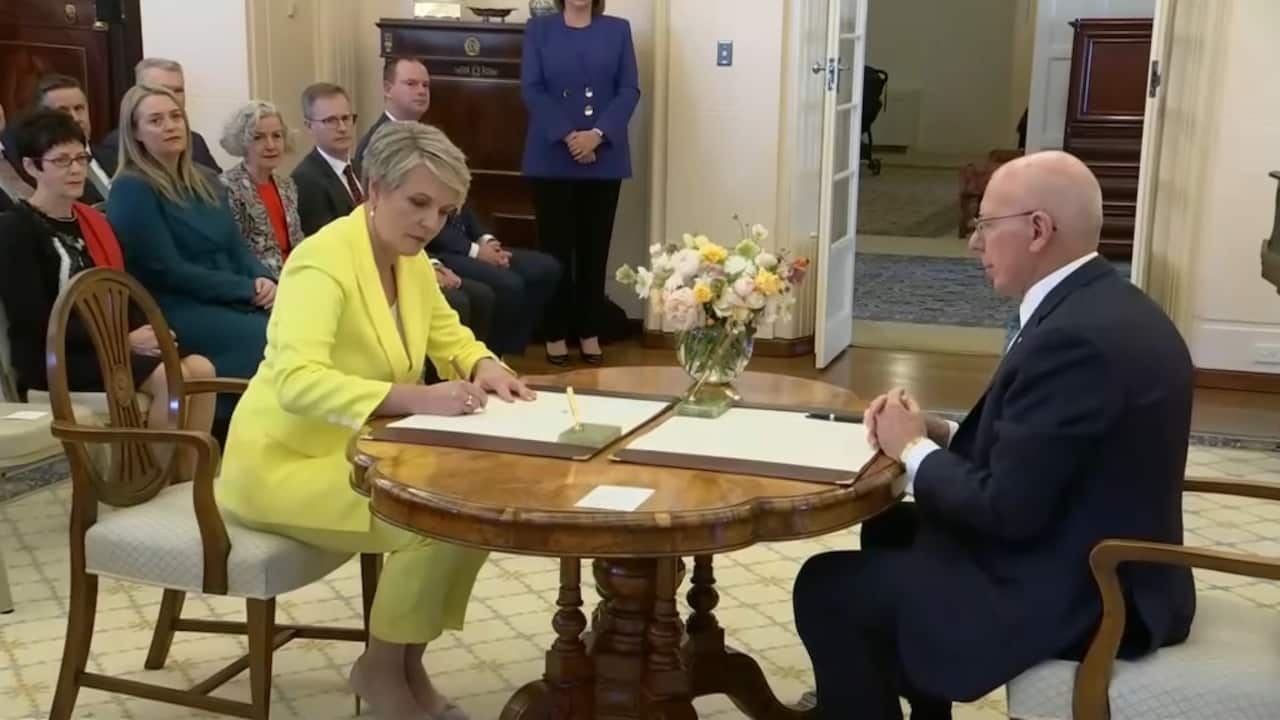 Tanya Plibersek wearing a yellow suit, sitting at table signing papers
