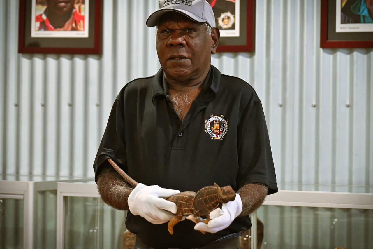 A man wearing white gloves holding a wooden lizard.