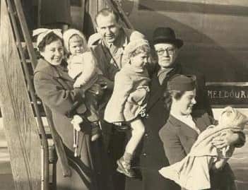 A grainy black and white photo showing four adults and three babies on the steps of an aeroplane. 