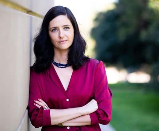 A woman wearing a crimson shirt standing next to a wall in a park.