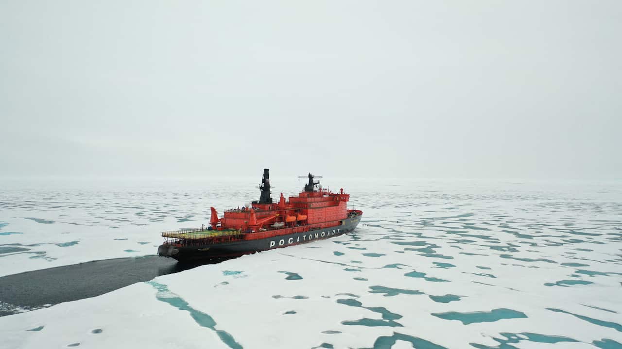 A Russian icebreaking vessell passes through a sheet of ice in a frozen landscape.