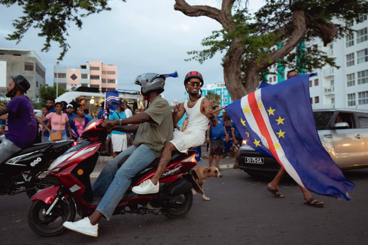 Two football fans on a motorbike wave the Cape Verde flag as they celebrate.