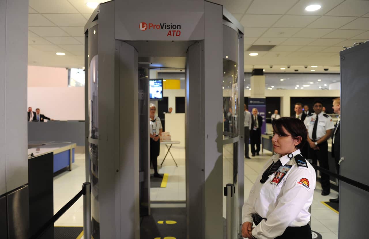 A large body scanner at an airport, with a security officer standing on the side. 