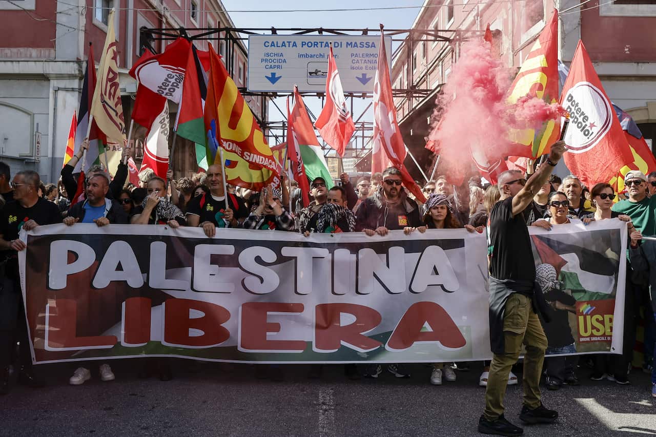 Protesters hold flags and a banner reading "Palestina Libera" at a rally.