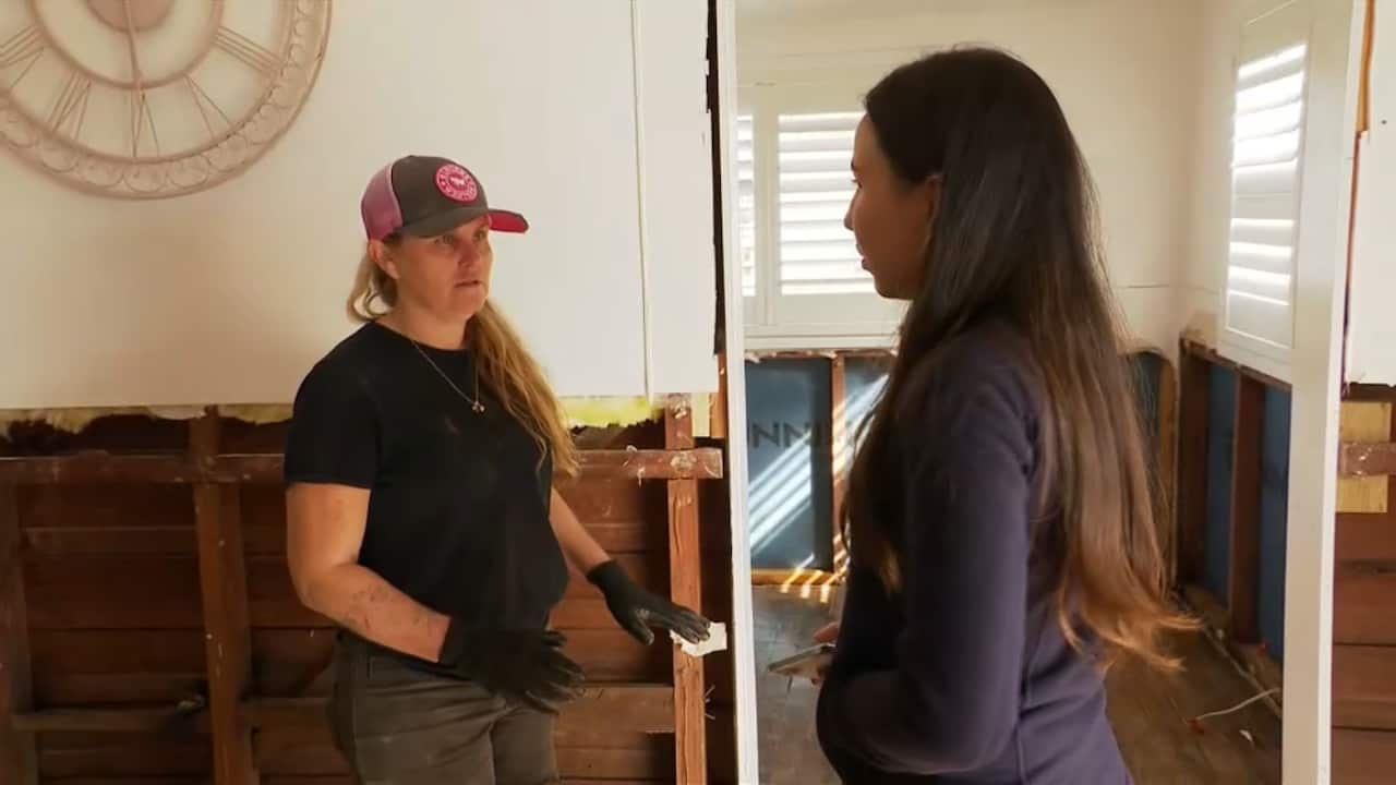 A woman with a hat and gloves speaking to a reporter inside a home