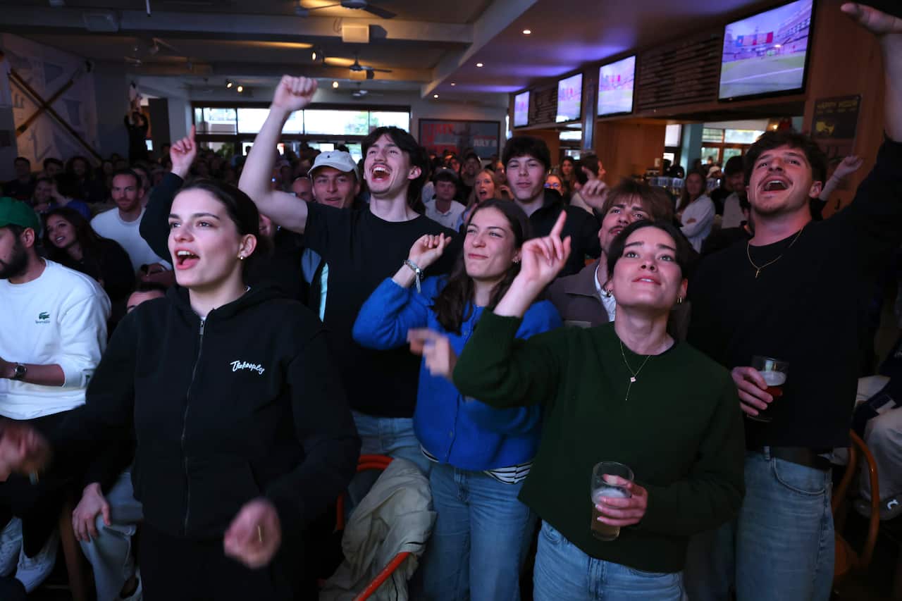 French football fans with hands in the air in a dark pub.