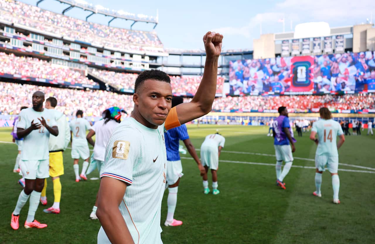 A French football player holding his left hand up in celebration on a football pitch