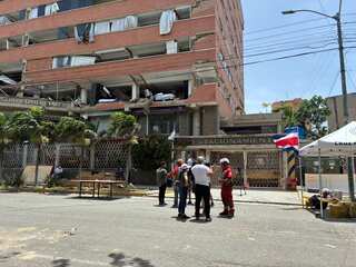 Rescuers stand in a circle on the street, with a partially demolished building behind them.
