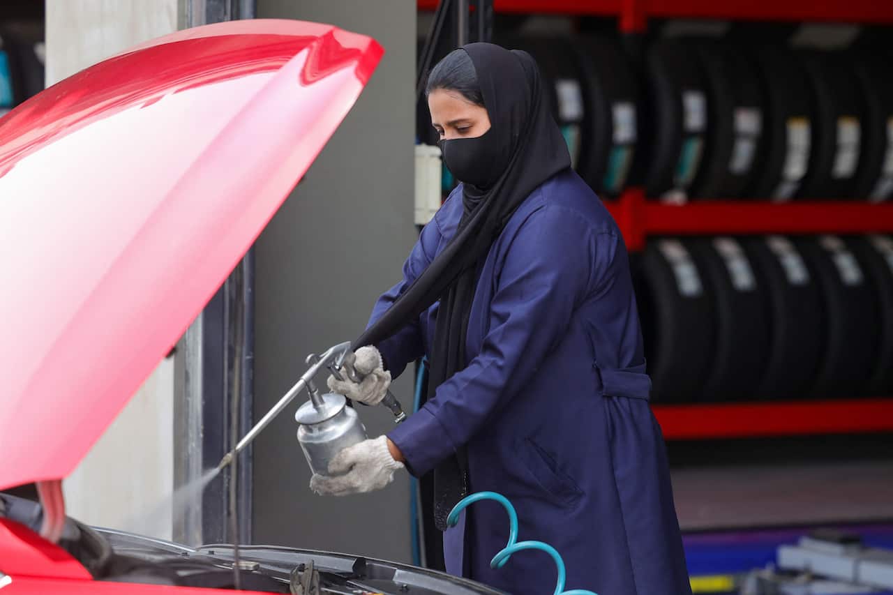 A woman in Saudi Arabia cleans a car's motor at an auto quick service garage in Jeddah City on May 26, 2022.