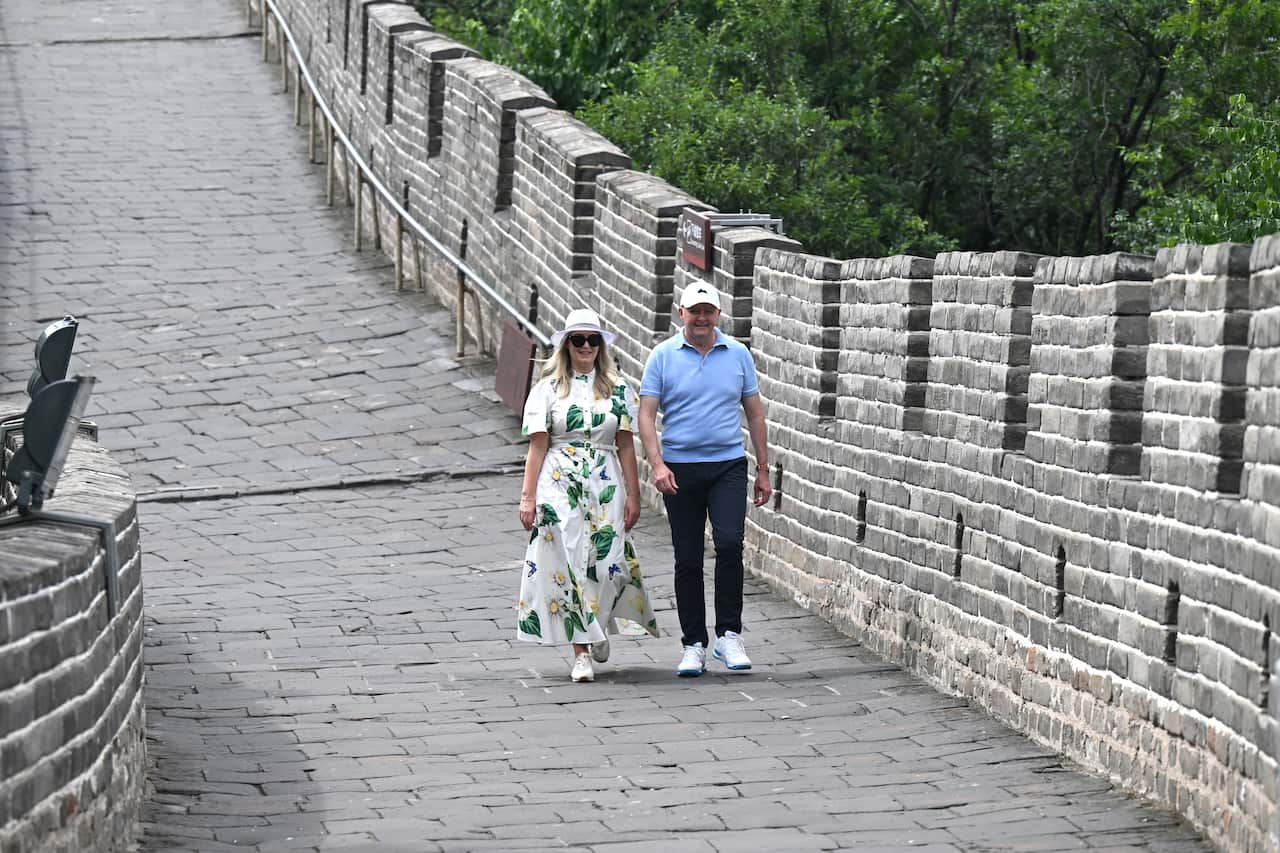 A man in a blue polo and a woman in a white and green floral dress walk along the Great Wall of China.