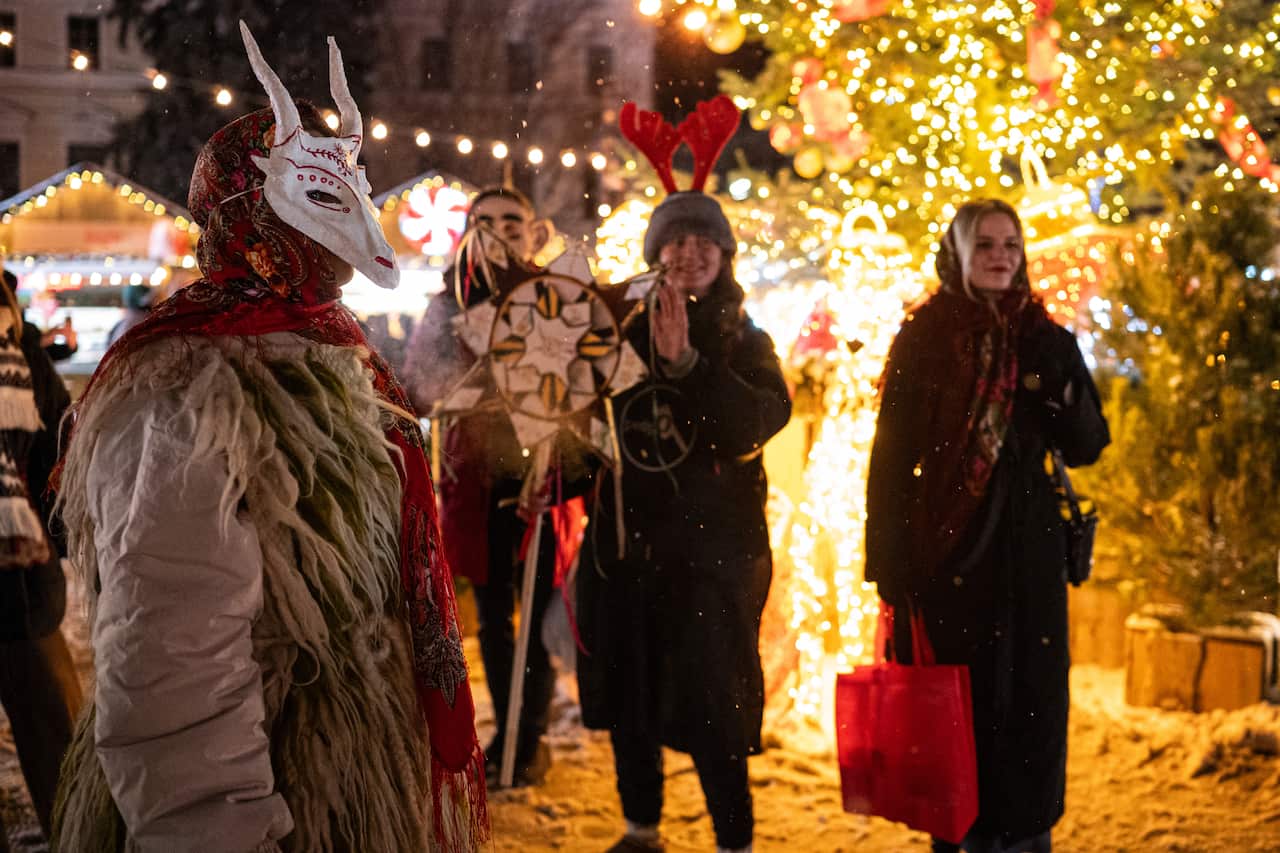 A festive outdoor marketplace with people dressed in warm clothes and masks.