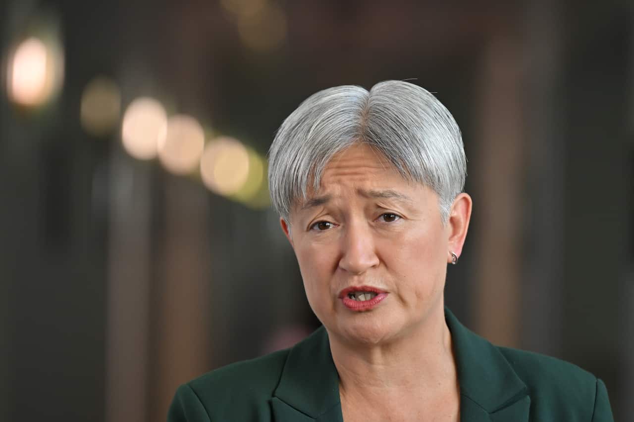 Penny Wong, wearing a green blazer, standing in a hallway.