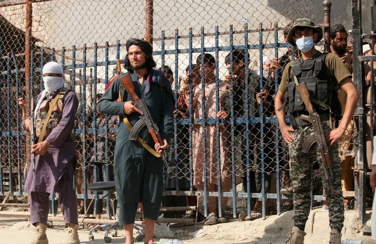 Three men in front of a fence holding guns. There are people behind the fence.