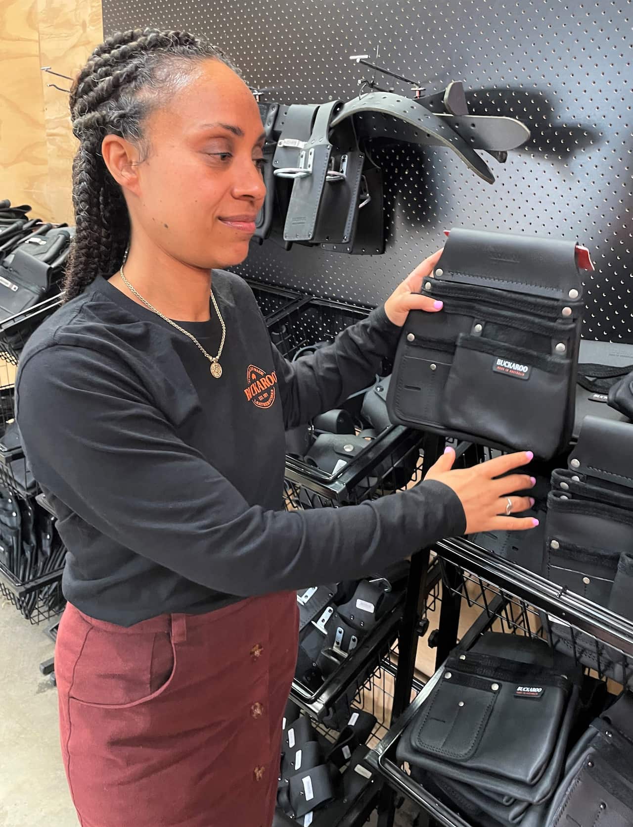 A woman in a black t-shirt stands next to a shelf holding a leather pouch.