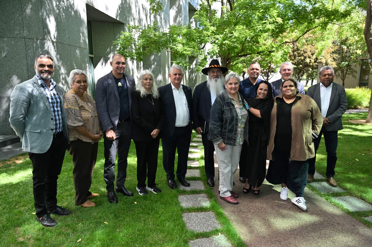 A group of Indigenous Australians stand in a courtyard.
