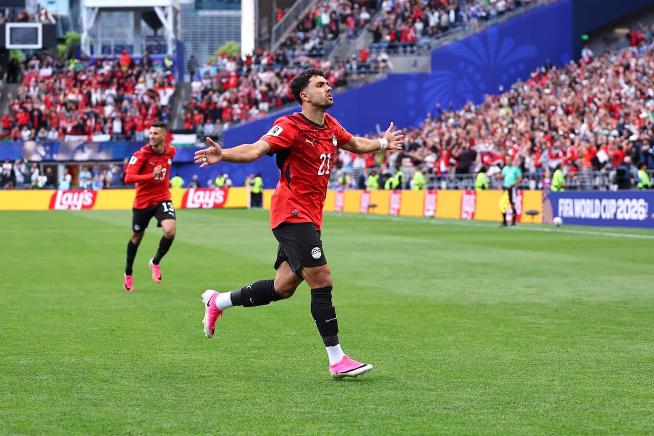 A football player in a red jersey running with his arms outstretched in celebration 