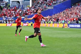 A football player in a red jersey running with his arms outstretched in celebration