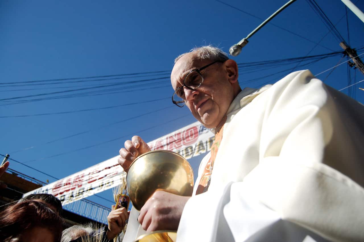 Cardinal wearing white clothing and holding a gold coloured chalice outside