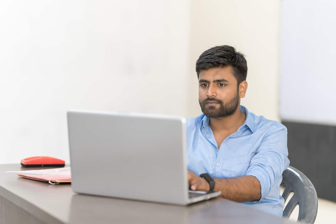 Young Indian Man using a laptop in a classroom.