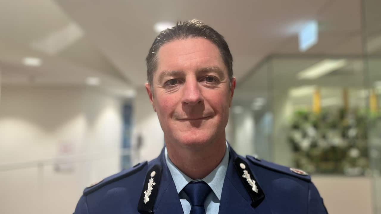 a middle aged man in police uniform smiles at camera in office