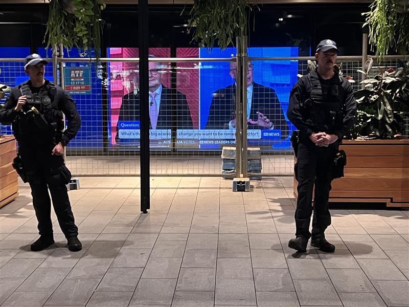 Police stand next to a fence with posters of two political leaders in the background.
