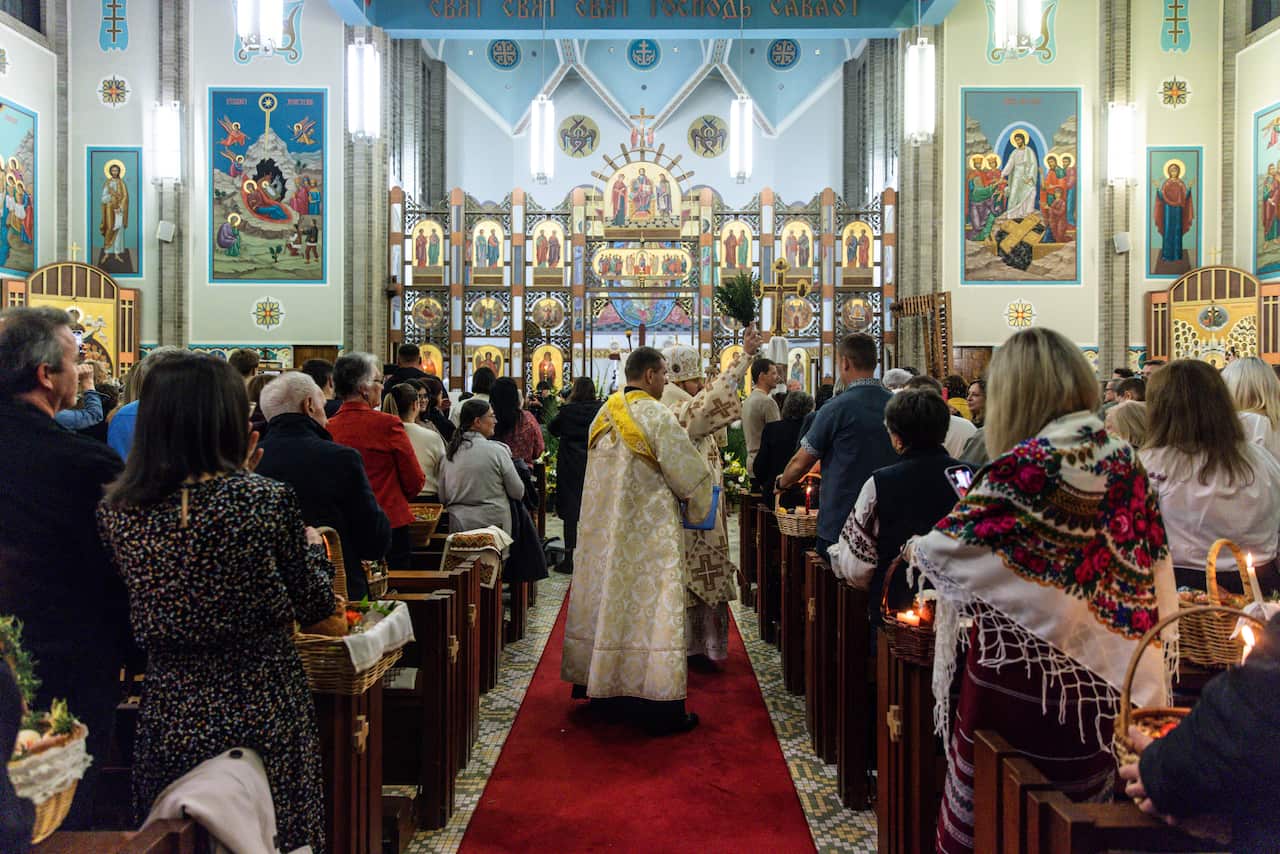 A priest holding a branch walks through the aisle of a church