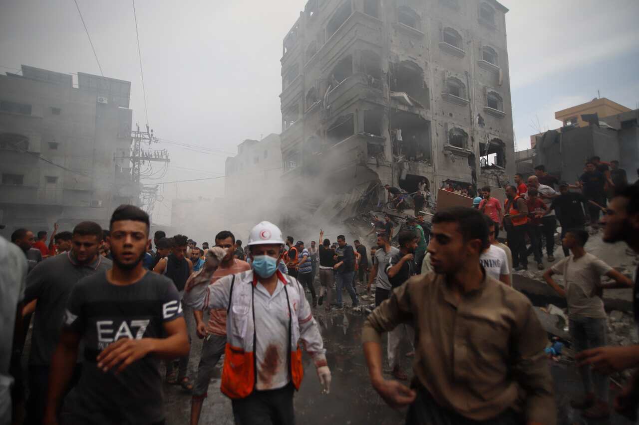 Crowds of people walking on the street. Behind them are destroyed buildings.