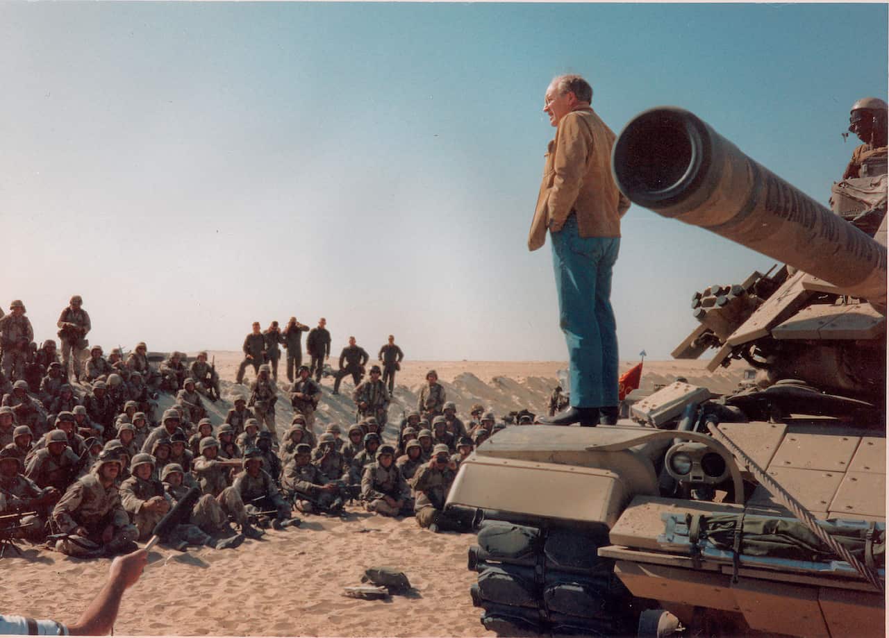 Man stands on a tank in front of group of soldiers