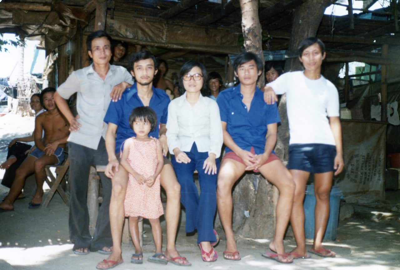 Vietnamese refugees, four men, one woman and one child, standing in a refugee camp in Malaysia. 
