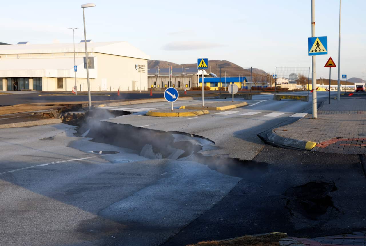 Steam rises from a fissure in an empty road next to a pedestrian crossing.
