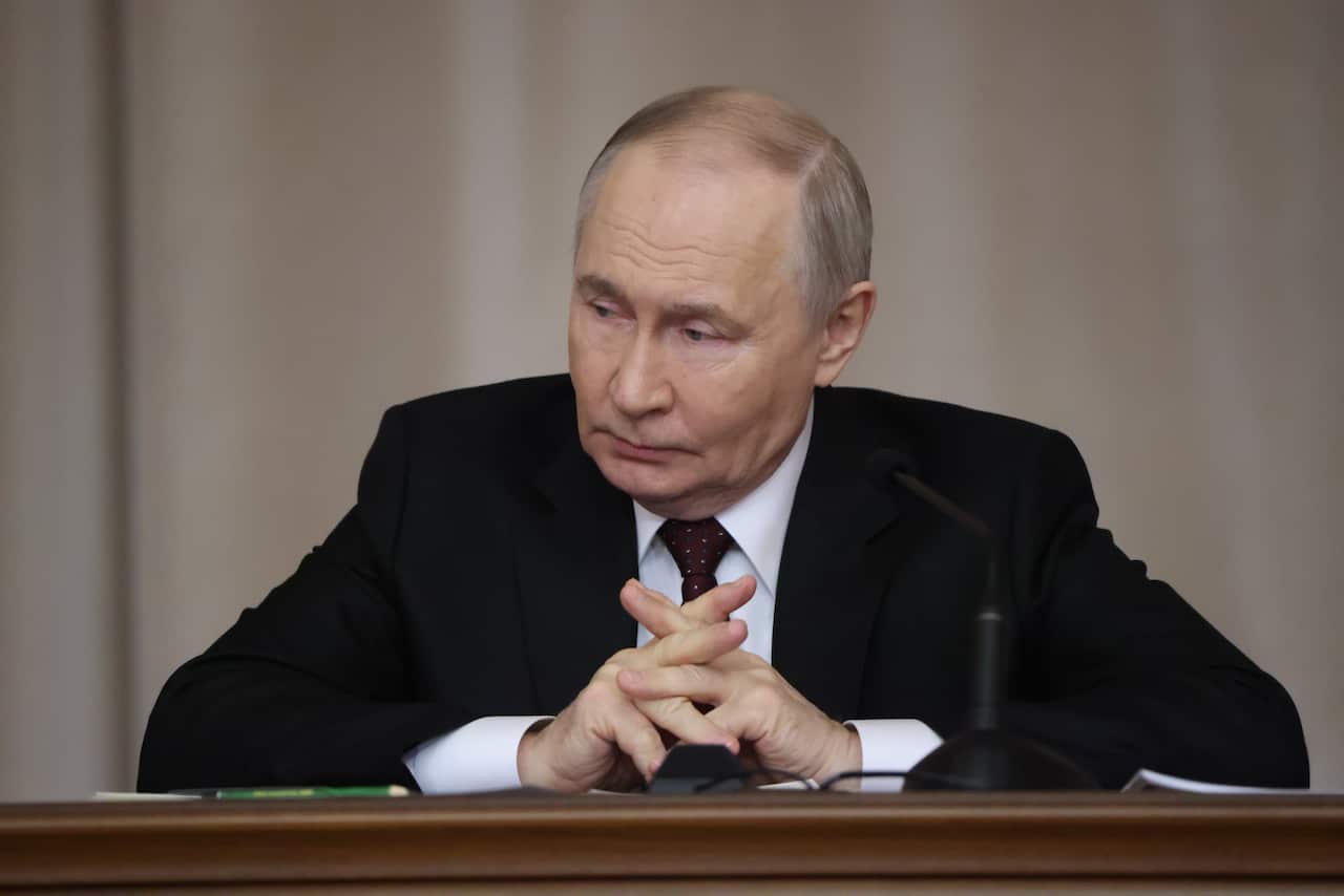 Russian President Vladimir Putin seated at a desk in front of a microphone.