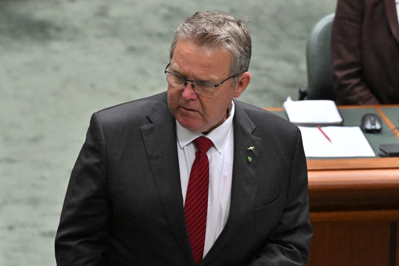 A grey haired men with glasses, looking to the side.