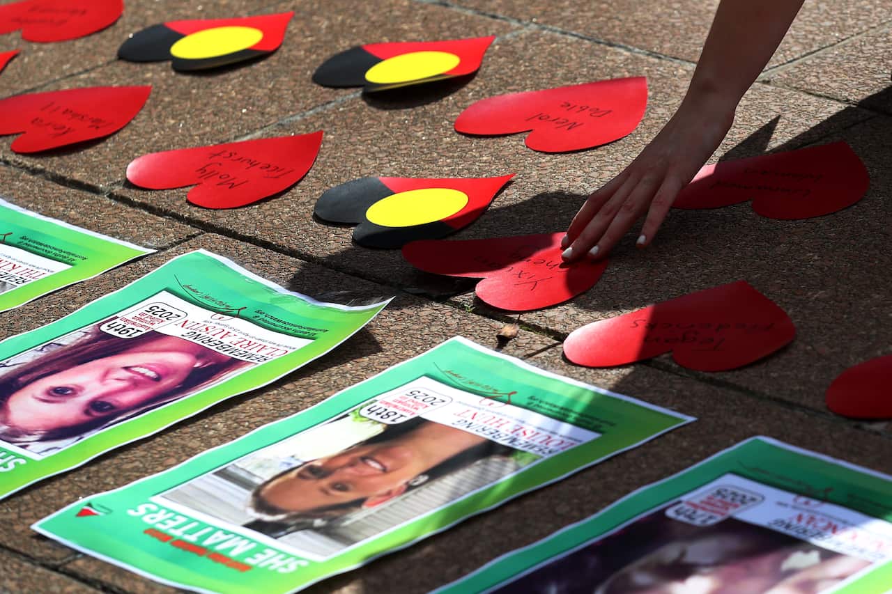 A hand places a red paper heart among flyers with women's photos and other red and black paper shapes.